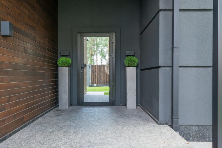 Contemporary entrance featuring a glass door, wooden walls, and elegant potted plants.